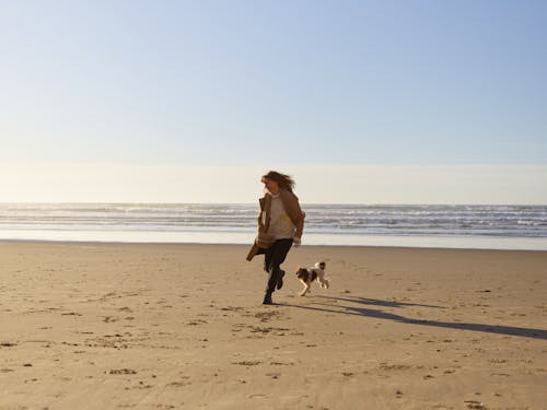 Free Woman and a Dog Running on Seashore Stock Photo