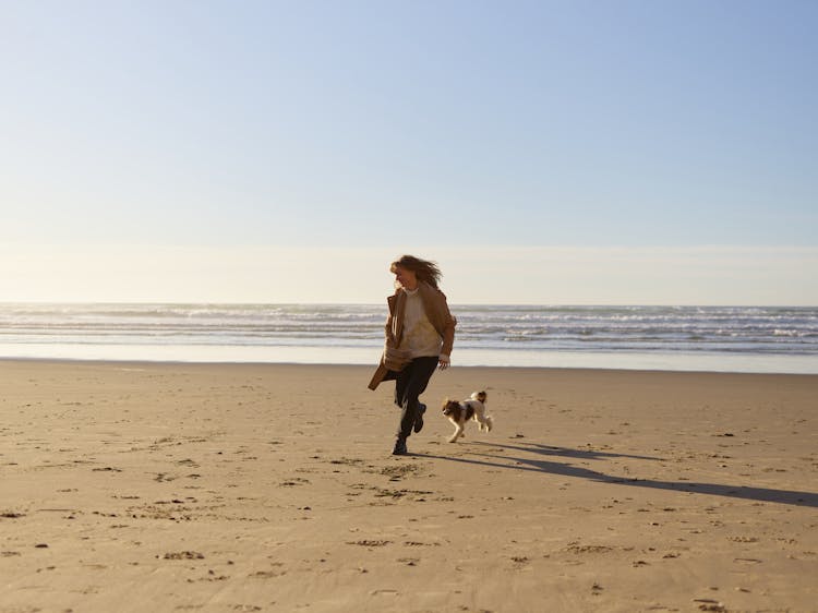 Woman And A Dog Running On Seashore