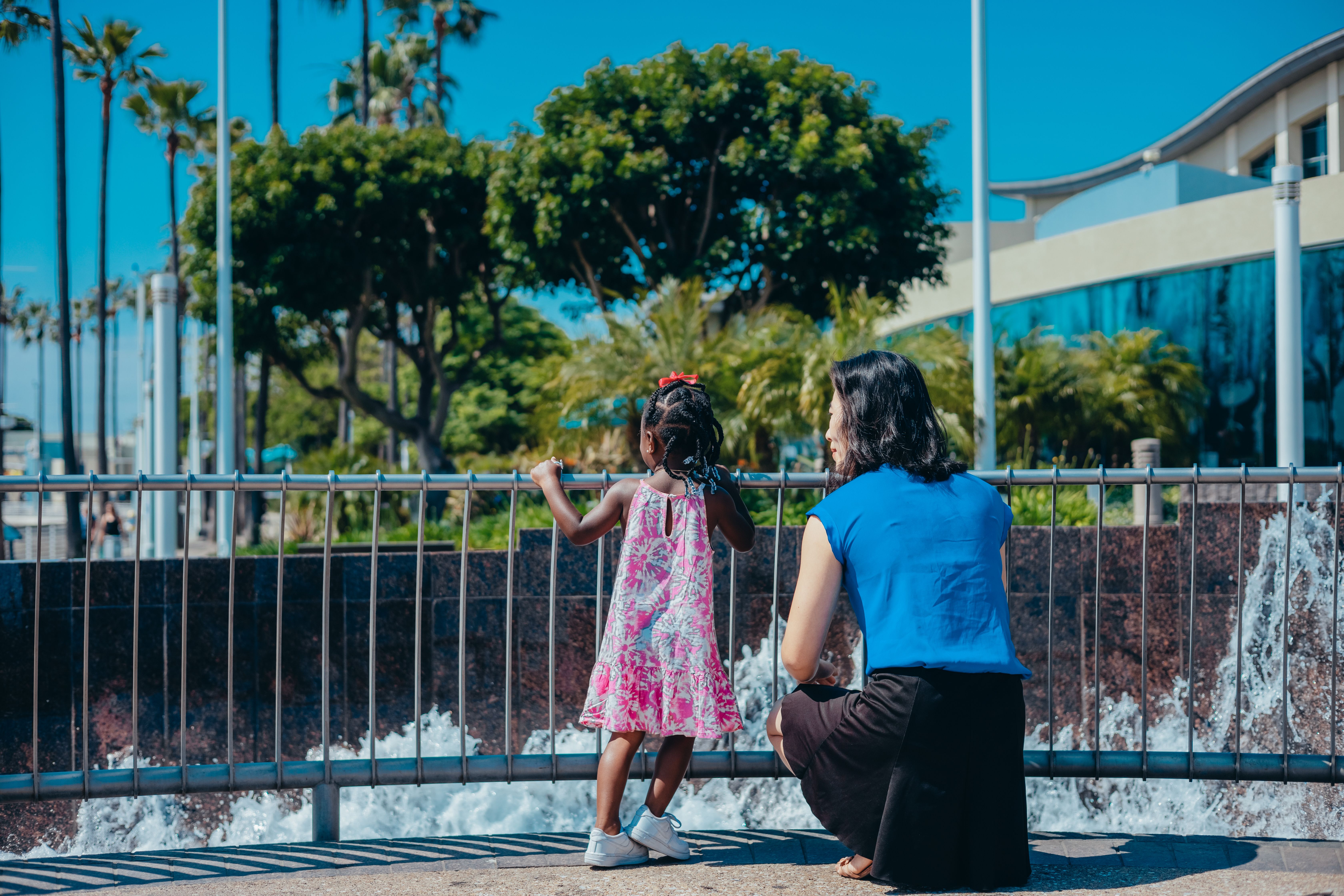 A mother and daughter enjoy a sunny day by the urban fountain, emphasizing family time.