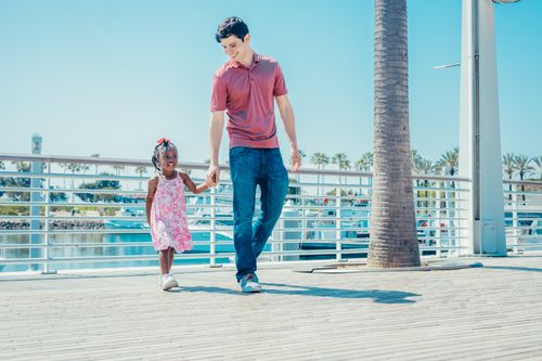 Free A dad and daughter enjoy a sunny walk by the marina, holding hands and smiling. Stock Photo