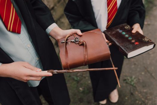 Two children in wizard costumes holding a wand and spell book outdoors, resembling magic school theme.