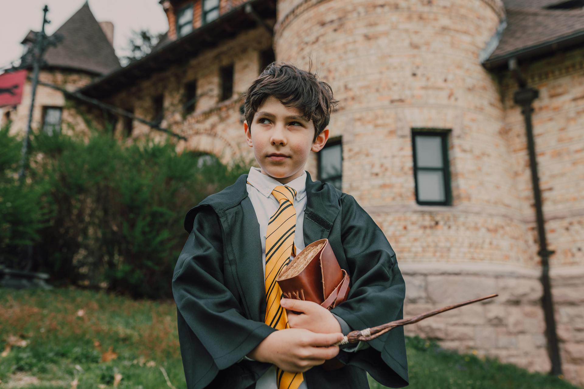 A Boy in Black Robe Holding a Wand and Spell Book