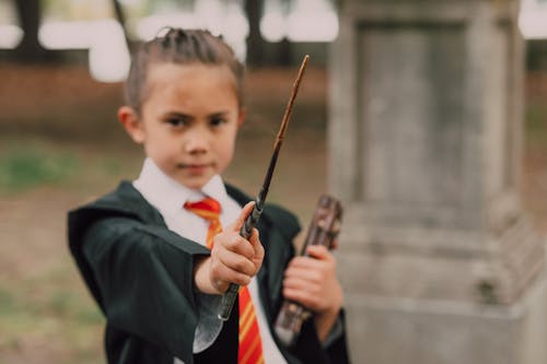 A Kid Holding Book of Spell and Magic Wand while Looking at the Camera