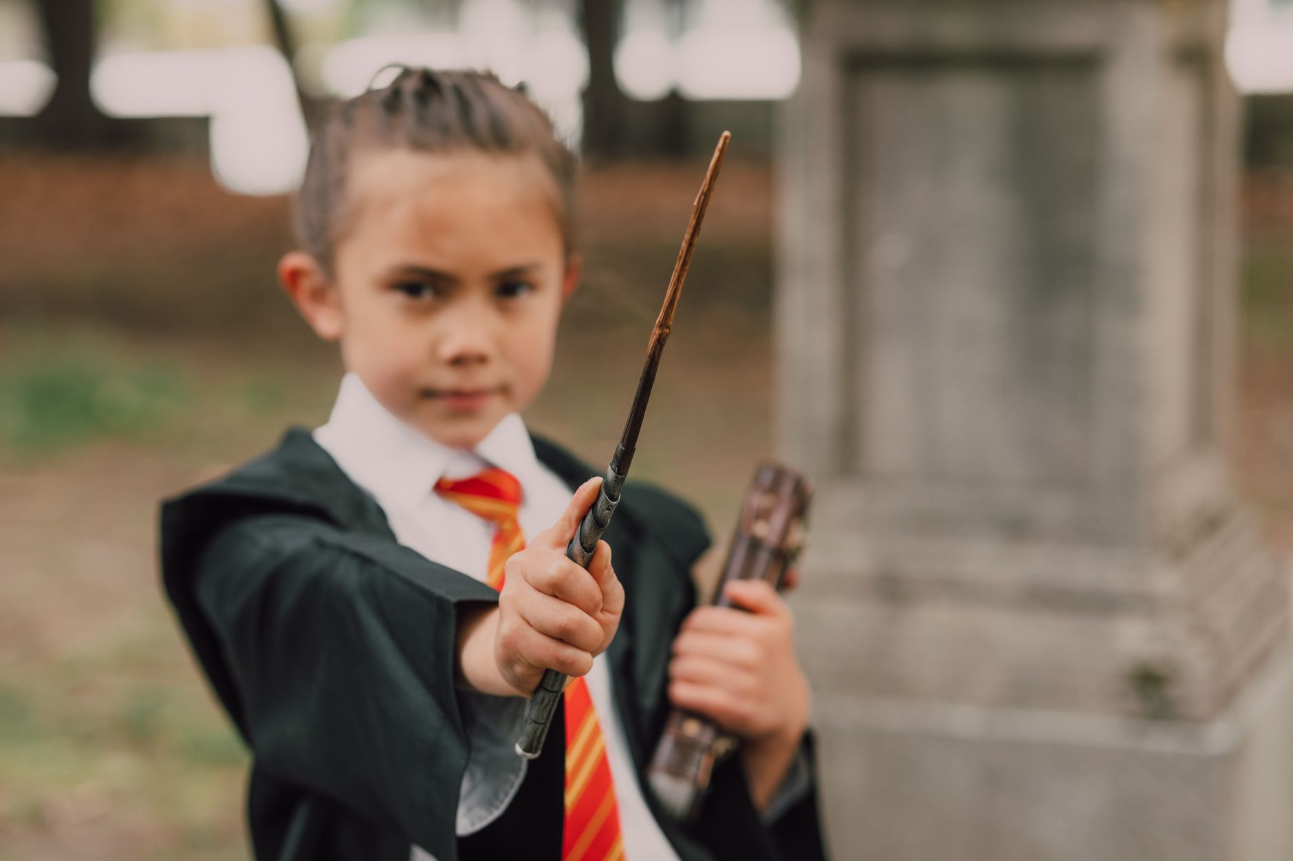 A young boy in a wizard costume holding a wand and book in an outdoor setting.
