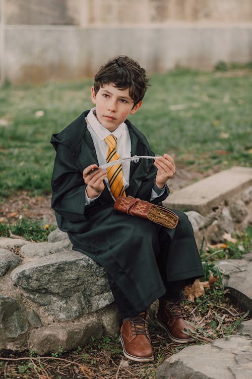 A Kid in Wizard Outfit Holding Wand and Spell Book while Looking Afar
