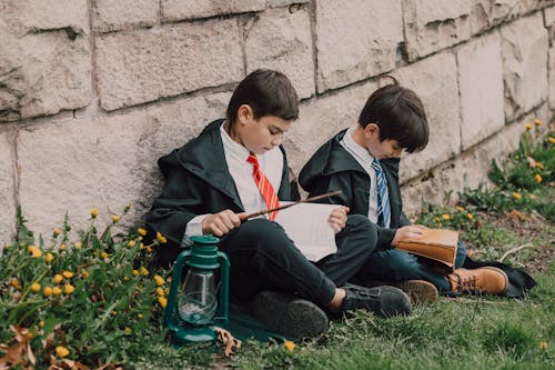 Boys Wearing Black Robes Sitting on the Ground while Reading a Book