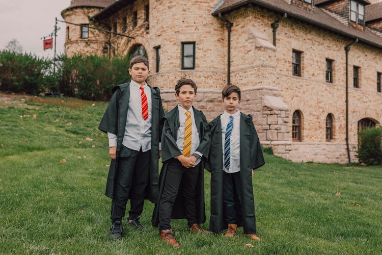 Boys In Black Robes Standing On Grass Near A Castle