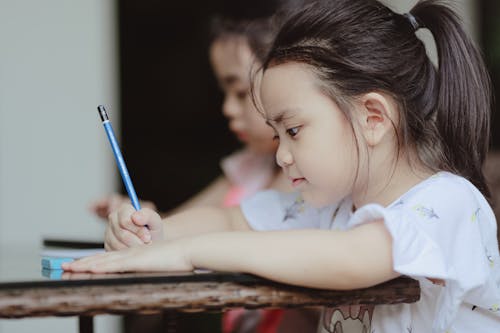 Free Adorable little Asian child girl drawing with pencil sitting at table in kindergarten Stock Photo
