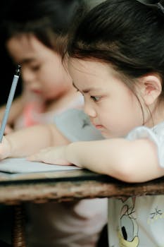 A young girl intently writing with a pencil in an indoor classroom environment.