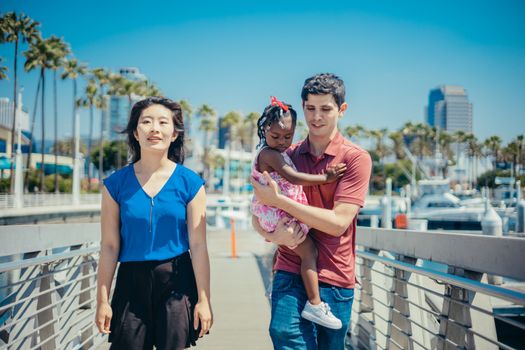Happy family walking on a marina boardwalk under a clear blue sky.