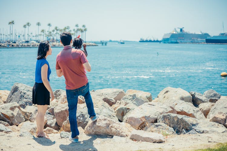 Interracial Family Standing Near Rocks On Beach Shore
