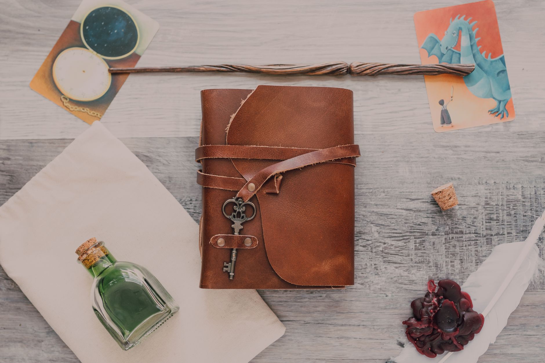 Enchanted flat lay featuring a leather journal, wand, potion, and mystical cards.