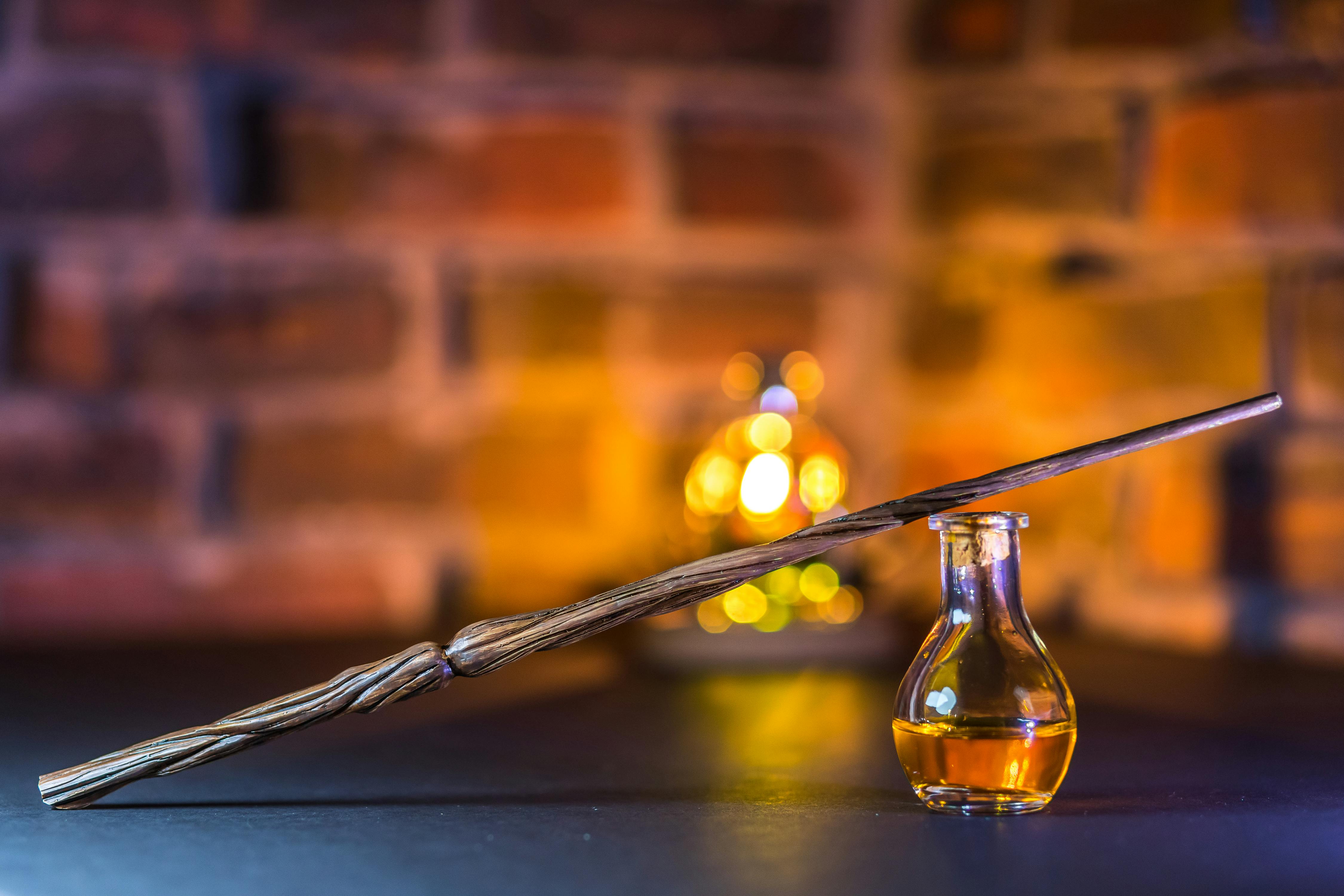 Close-up of a wooden wand balanced on a potion bottle with a warm, brick wall backdrop.