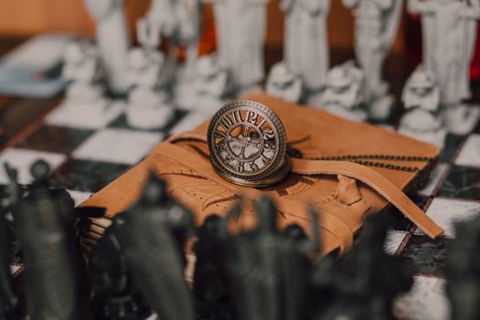 A steampunk clock rests on a leather-bound notebook with chess pieces in the background, evoking a magical atmosphere.