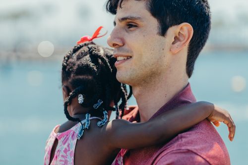 Free A heartwarming scene of a father embracing his daughter by the sea with a blurry background. Stock Photo