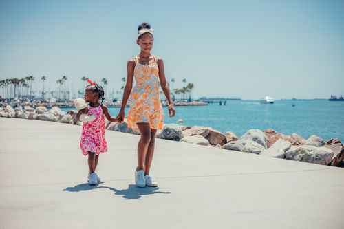 Free Young sisters walking hand in hand by the ocean on a sunny day. Stock Photo