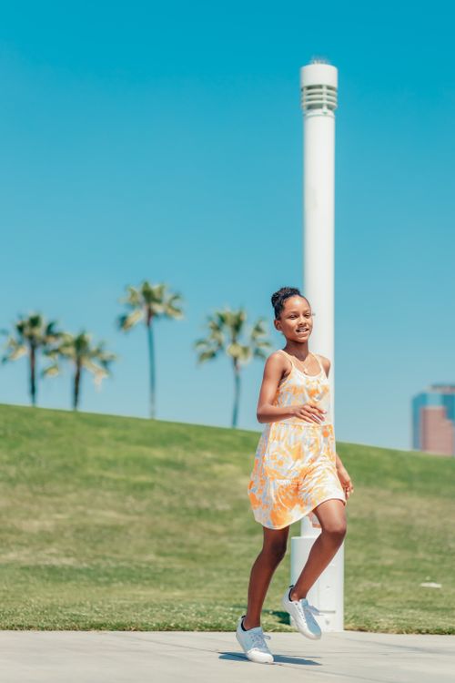 Free Smiling young girl enjoying a run in a sunny park with palm trees. Stock Photo
