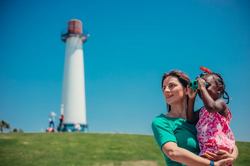 Free A woman and a child with binoculars near a lighthouse on a sunny day. Stock Photo
