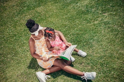 African American Girls Reading Book on Grass