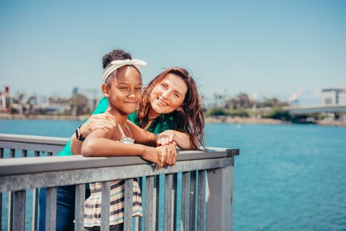 Free A smiling mother and daughter enjoying a sunny day by the waterfront with blue skies. Stock Photo