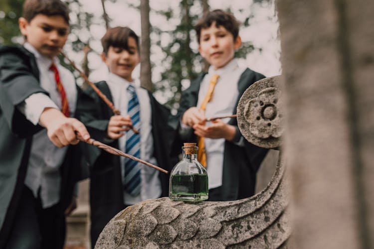 Three Boys In Black Robes Holding Wands