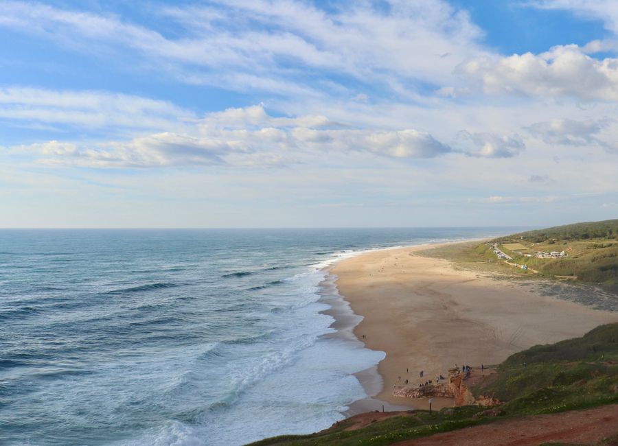 Serene coastal landscape of a sandy beach with gentle waves and a bright sky in Leiria District, Portugal.