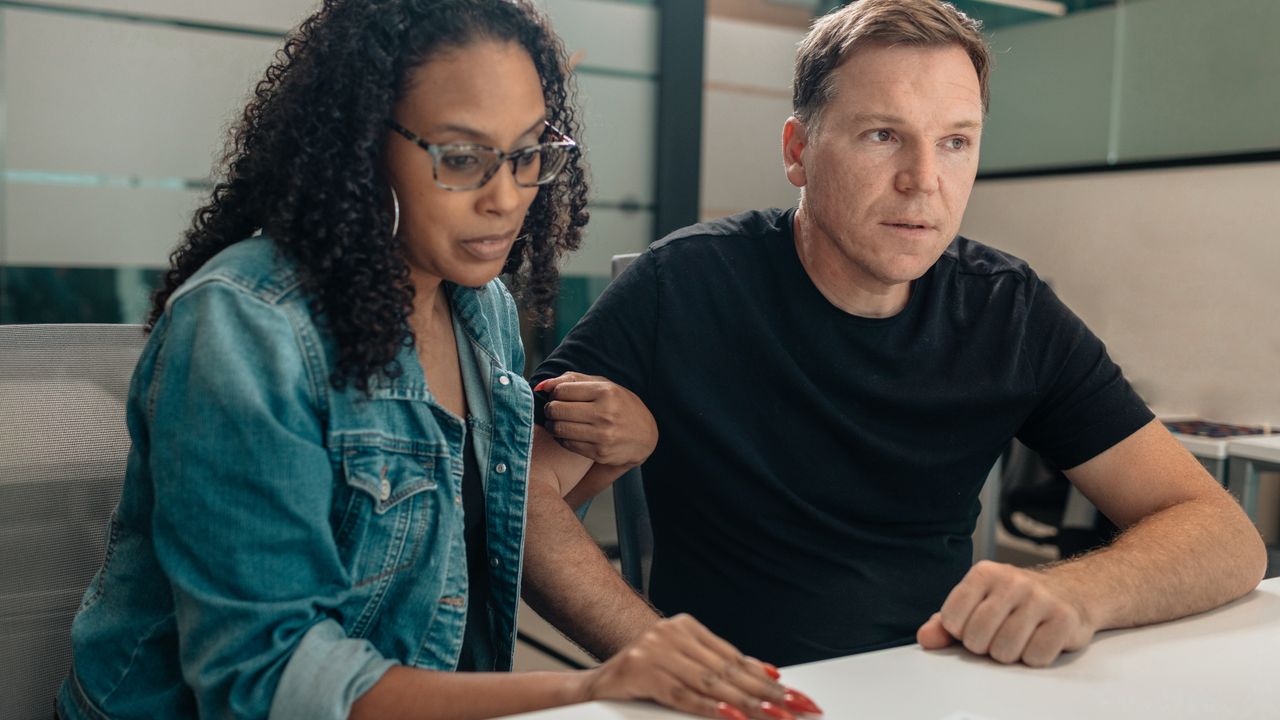 A couple closely examining paperwork in a modern office space. Focused and serious mood.