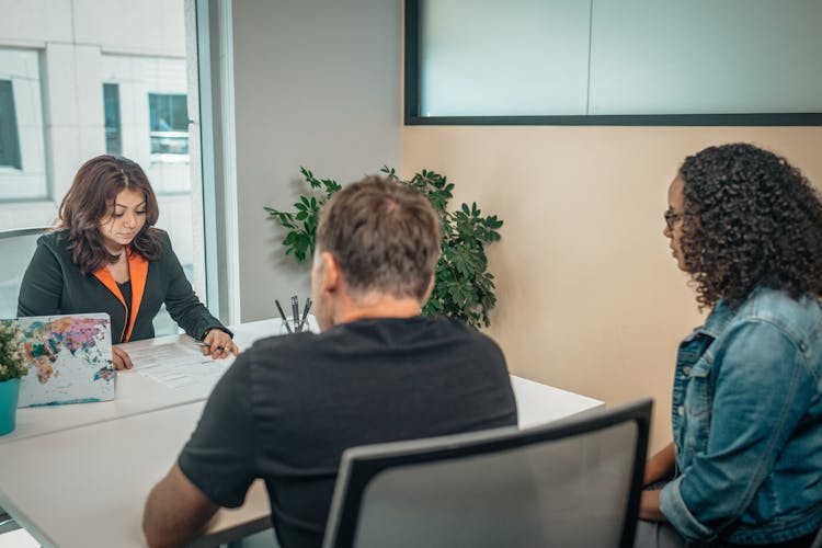 Black Employee Talking To Multiethnic Clients At Table In Office