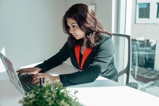 Focused woman working on a laptop in a bright modern office setting.