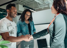 Smiling couple shaking hands with advisor in modern office.