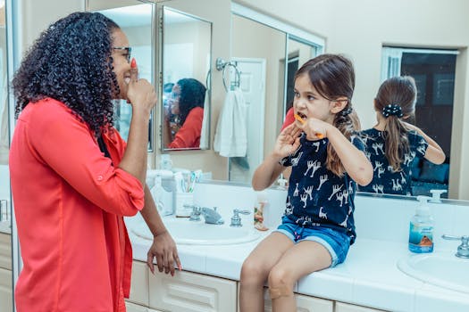 A mother teaches her daughter dental hygiene as they brush their teeth together in the bathroom.