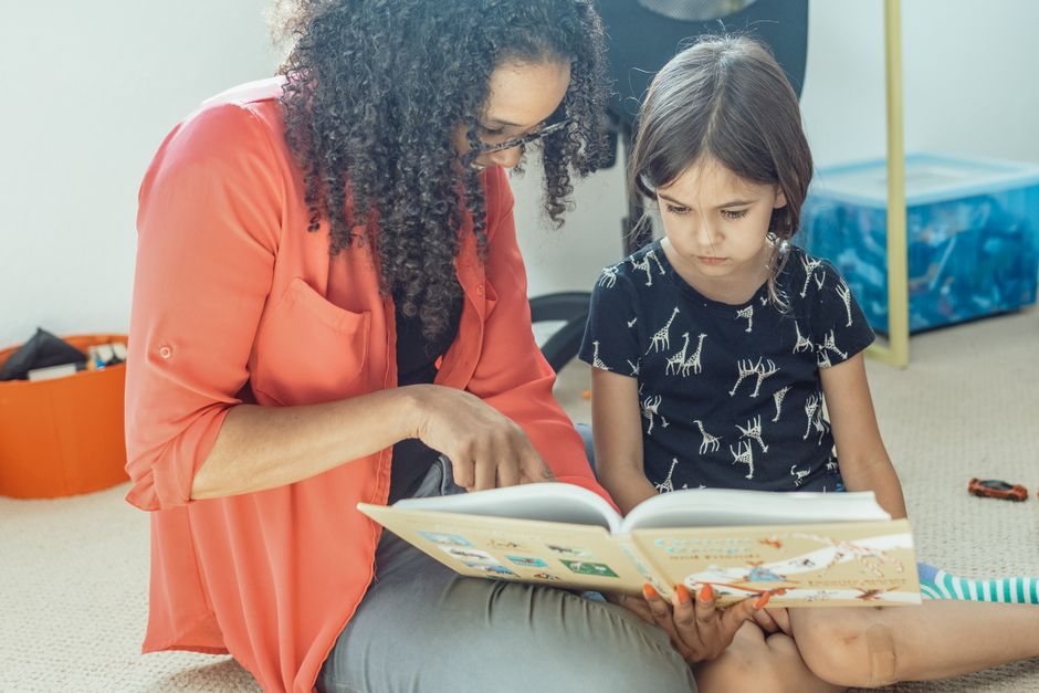 A mother and daughter share a bonding moment reading a book together at home, fostering love and learning.