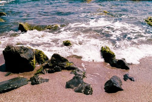 Free A tranquil beach scene with moss-covered rocks and gentle waves crashing on the shore. Stock Photo