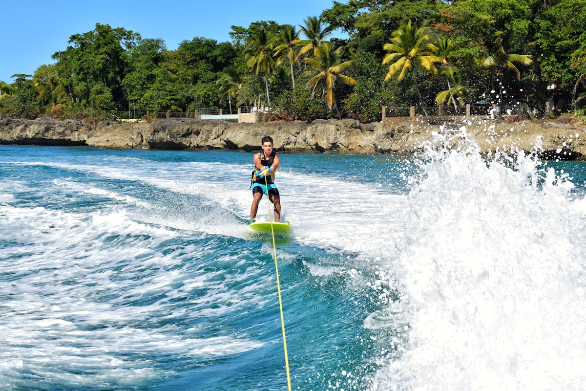 Hombre disfrutando esquí acuático en aguas azules tropicales, rodeado de vegetación exuberante