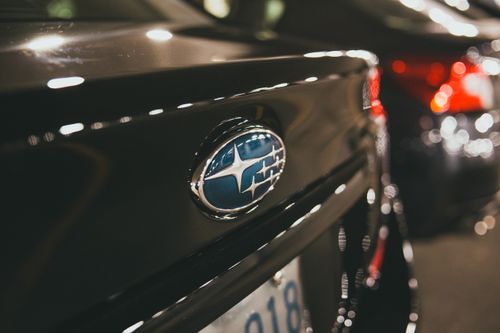 Free Close-up shot of a Subaru car emblem with a blurred parking lot background, showcasing automotive branding. Stock Photo
