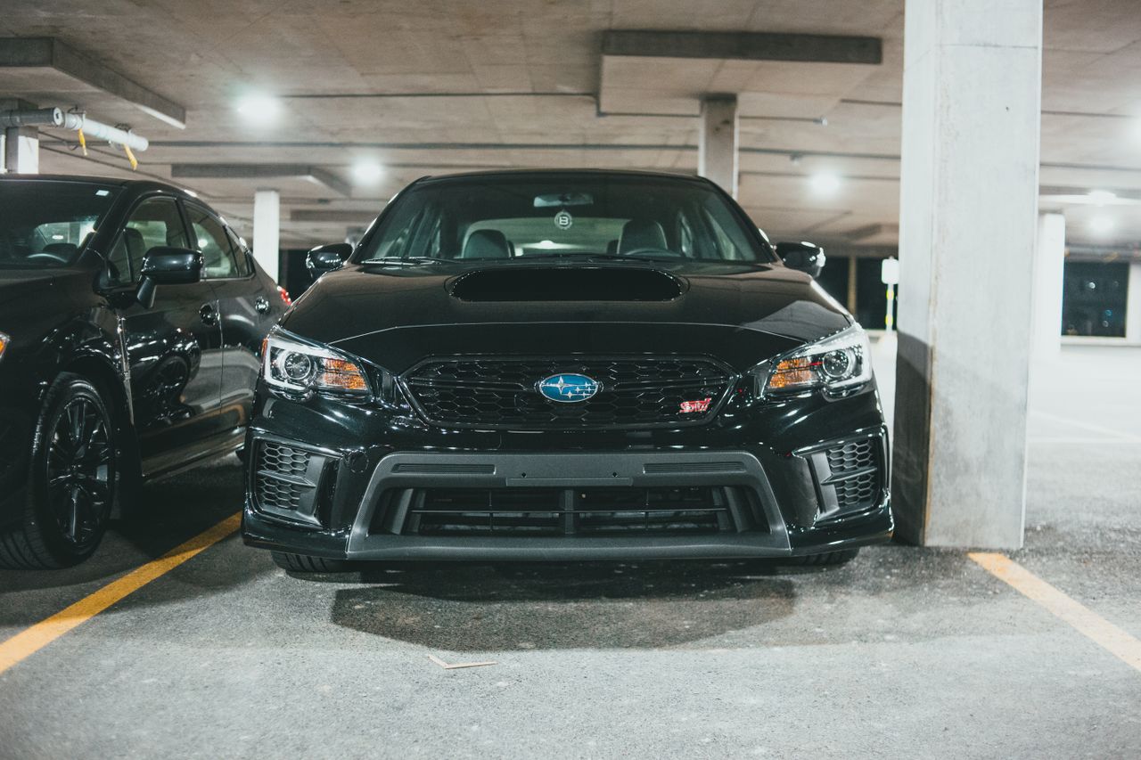 front view of a black subaru sedan in a well lit indoor parking garage