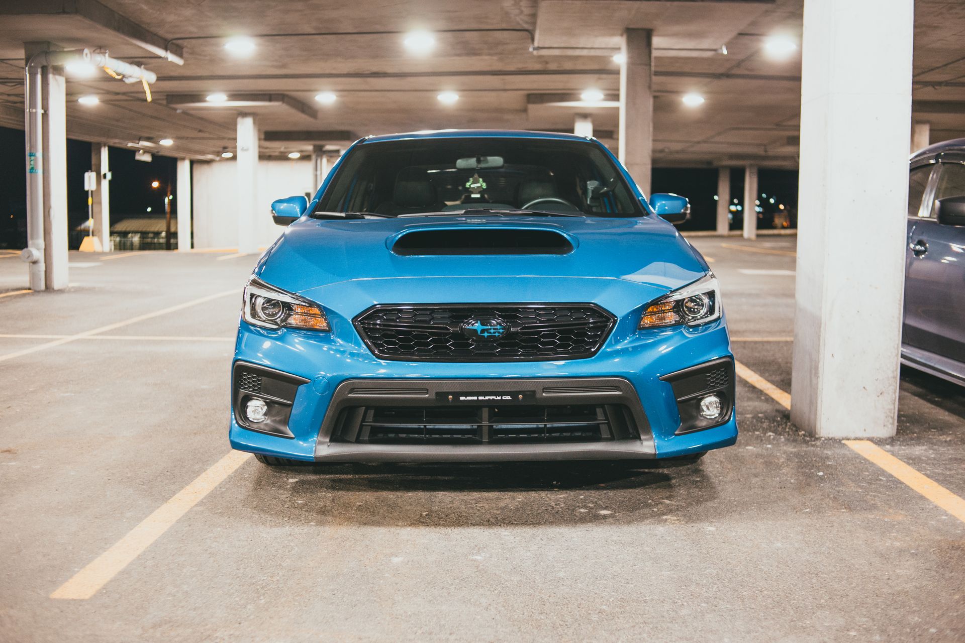 Blue Subaru parked in a well-lit urban parking structure at night, showcasing automotive details.