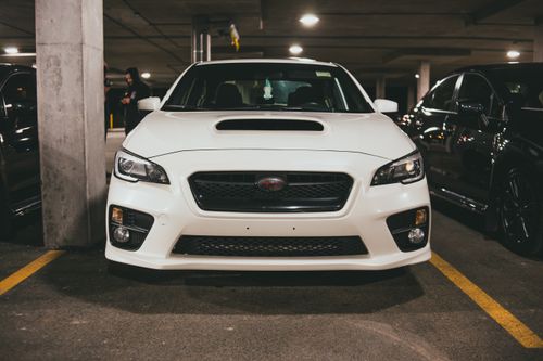 Free A sleek white car parked in a dimly lit urban garage, front view. Stock Photo