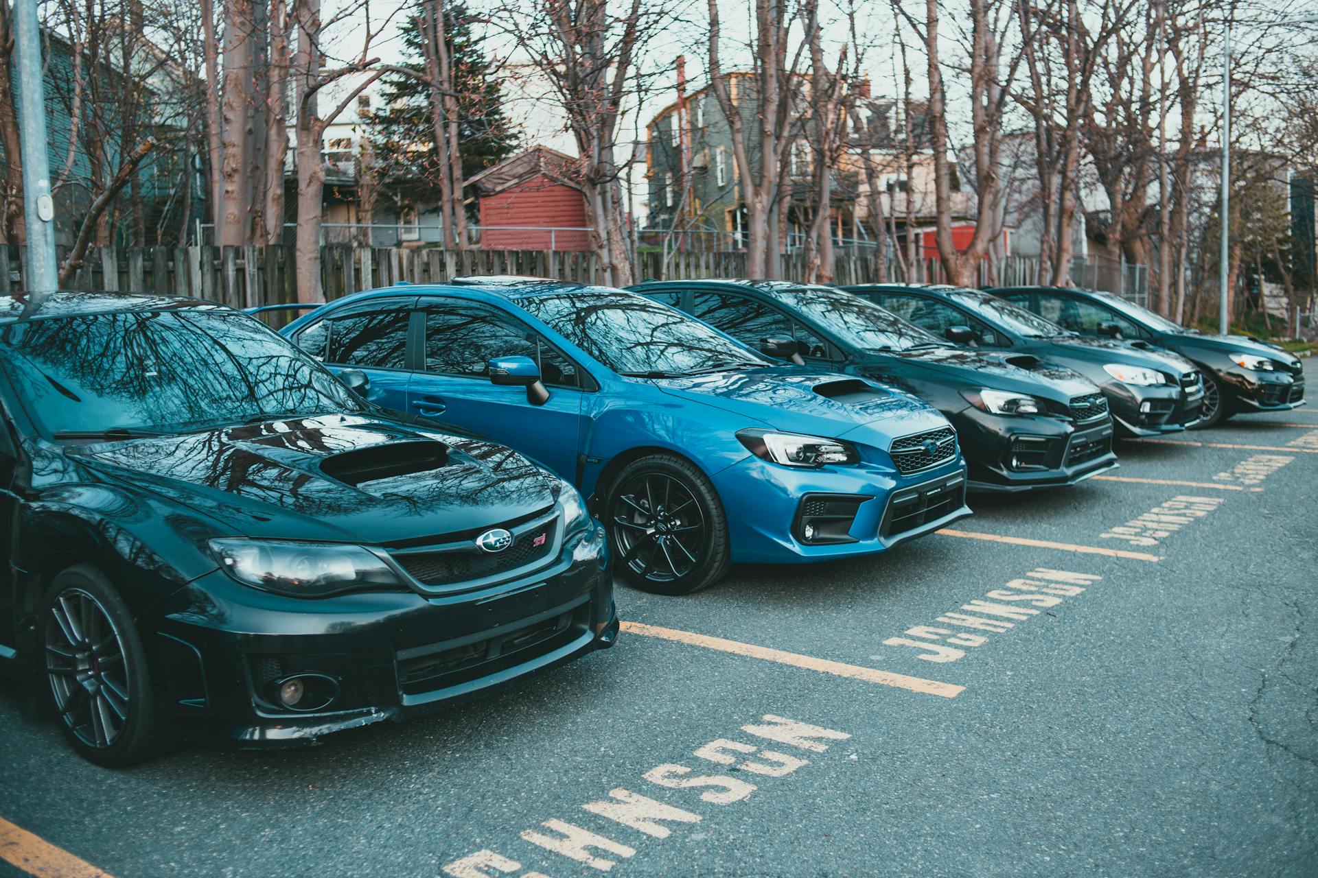 Multiple Subaru cars parked in an outdoor lot lined with trees, showcasing automotive design.