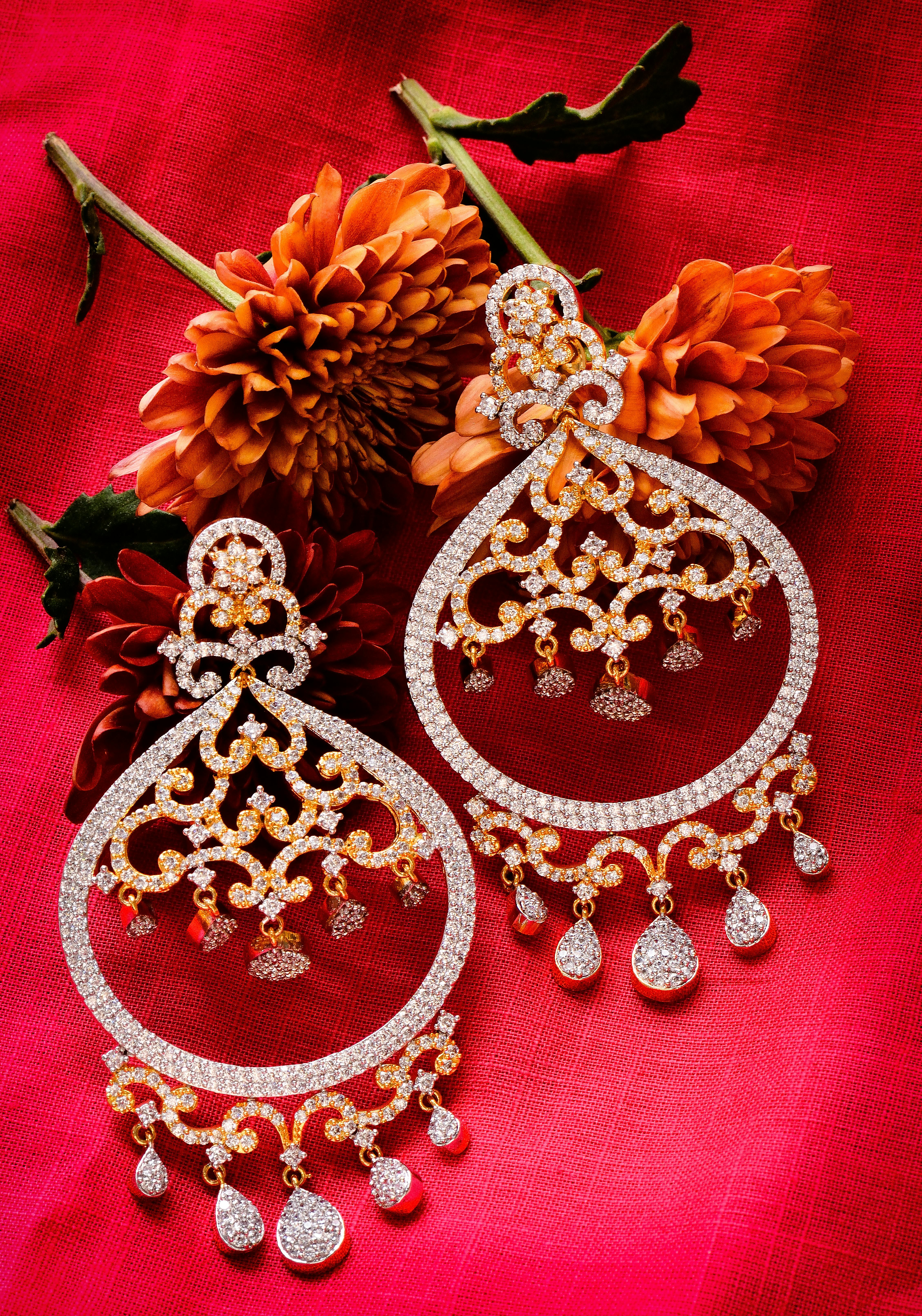 Exquisite diamond earrings set against a vibrant red background paired with blooming dahlias.