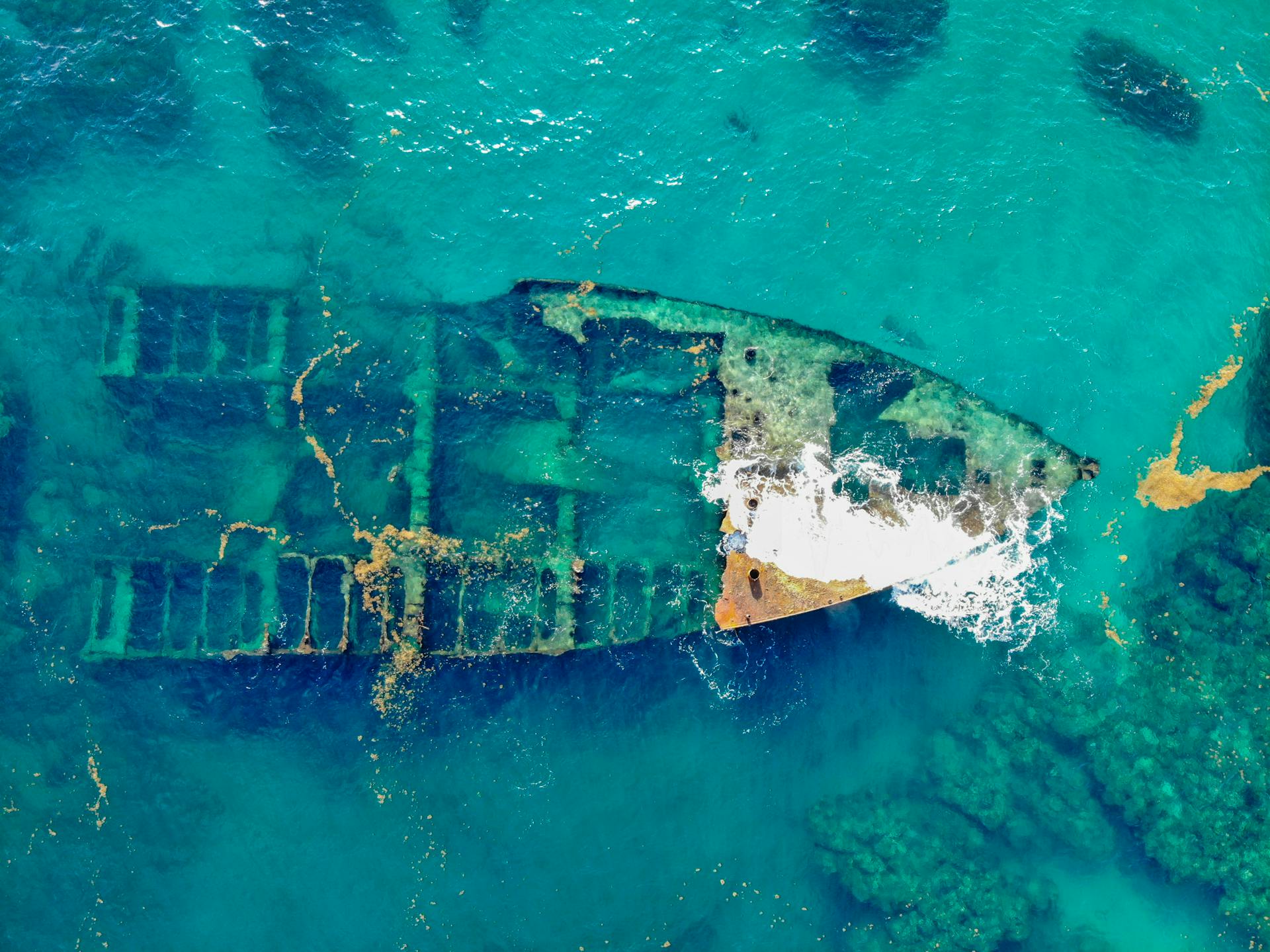 A stunning aerial view of a rusty sunken shipwreck submerged in clear turquoise waters.