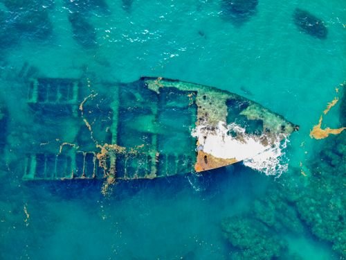 Free A stunning aerial view of a rusty sunken shipwreck submerged in clear turquoise waters. Stock Photo