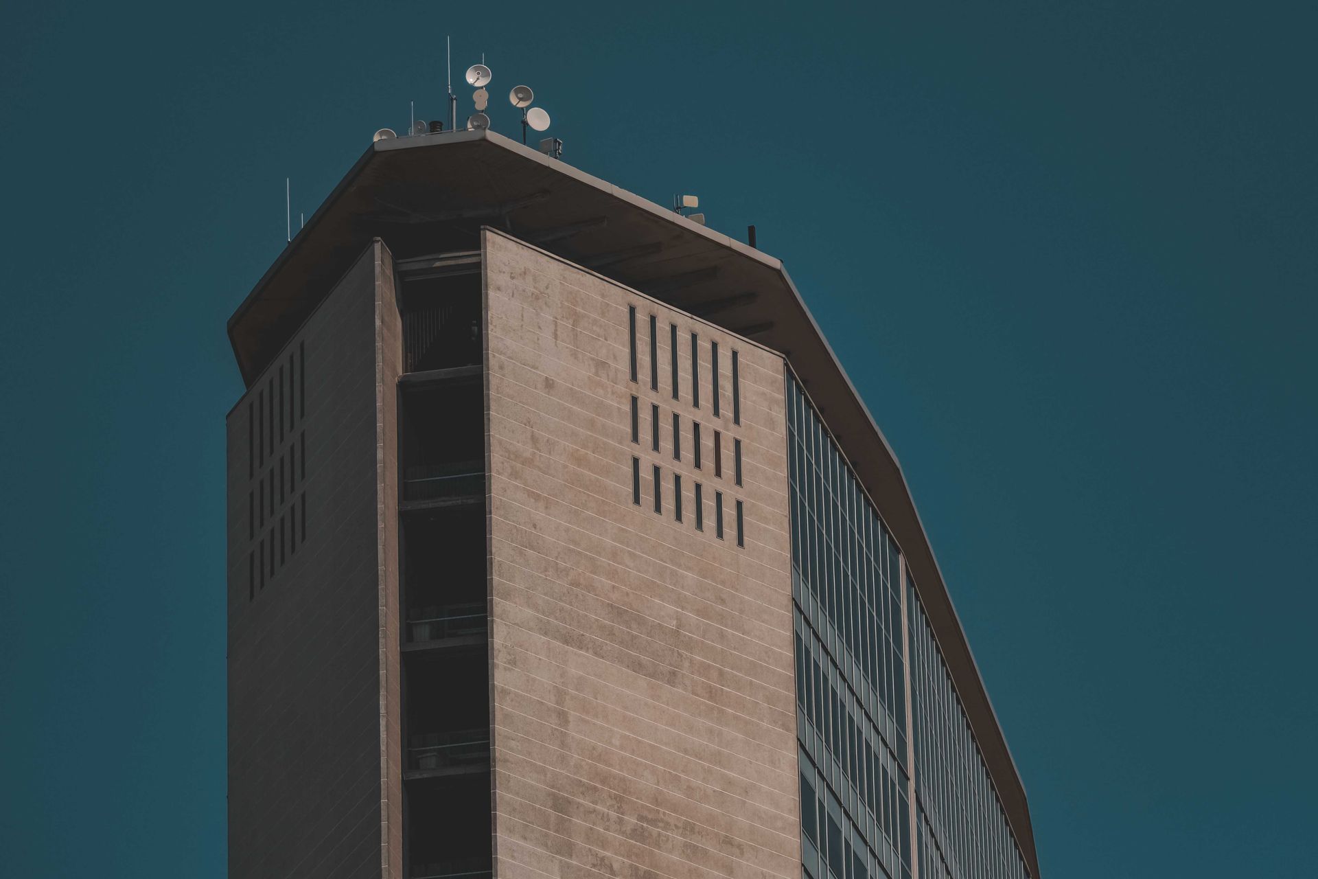 Urban high-rise building with unique design elements and satellite dishes against a clear sky.