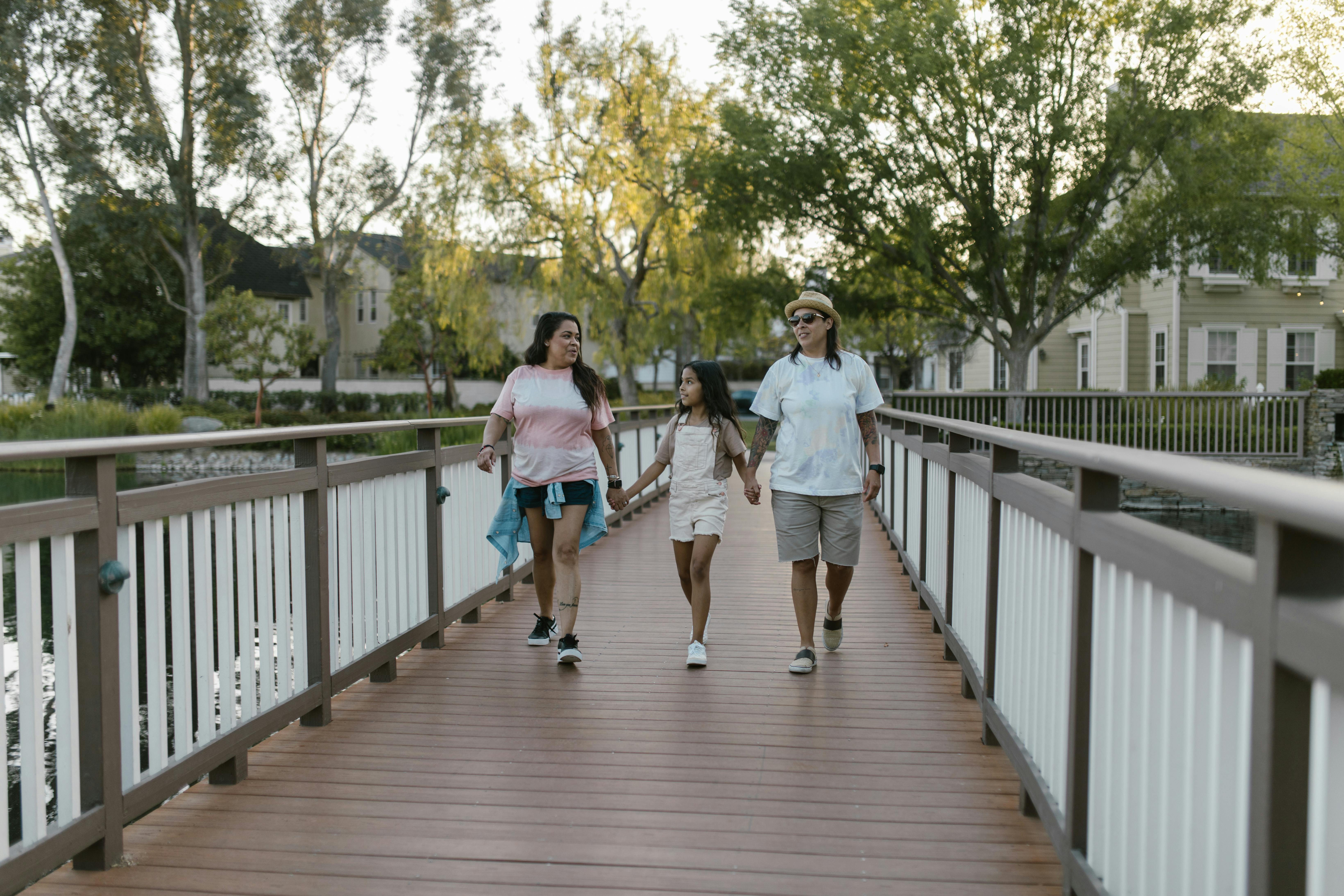 daughter holding hands with her mothers and walking on a bridge