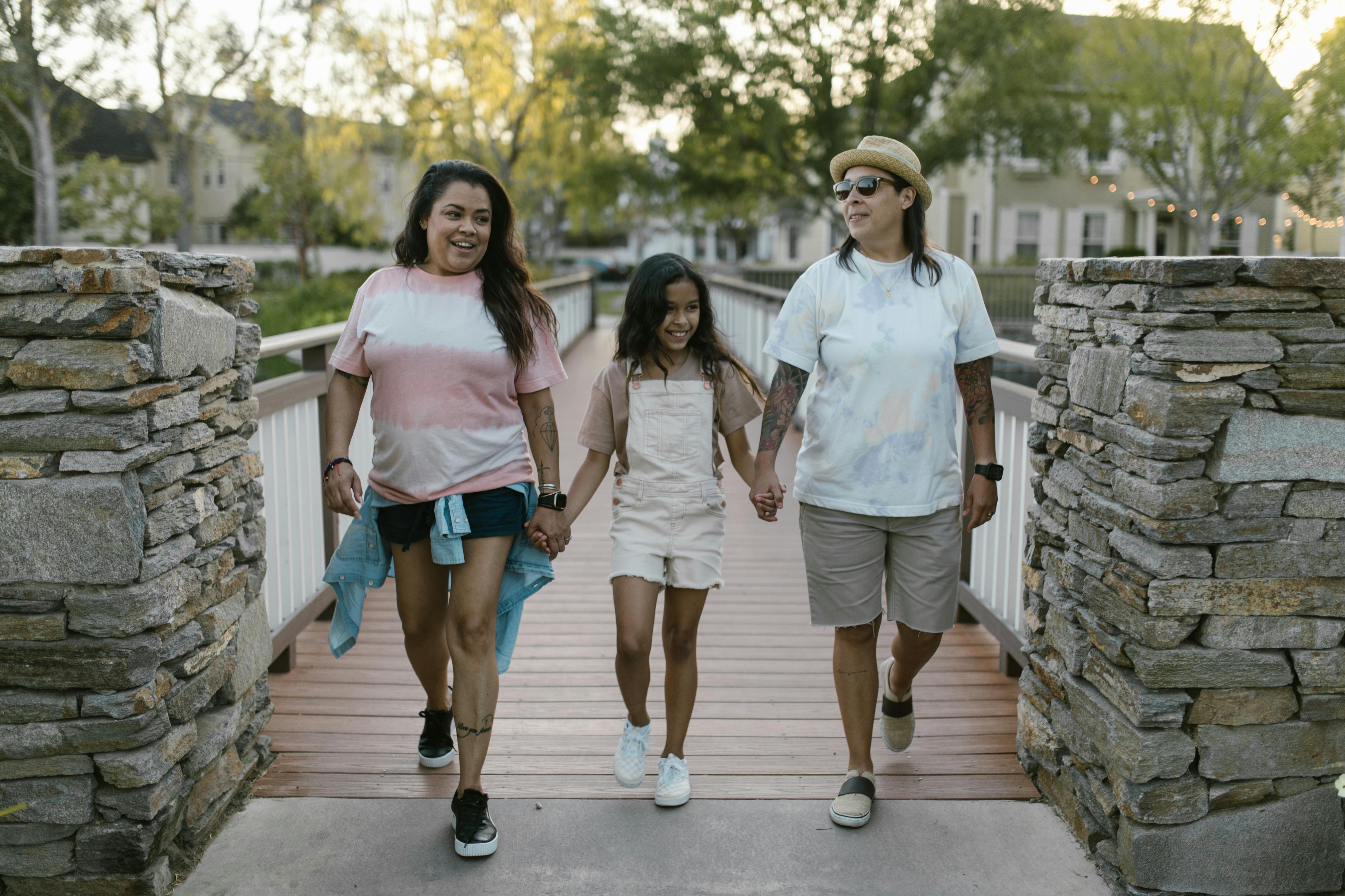 mothers holding hands with their daughter and walking on a bridge