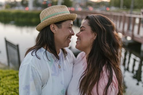 Free Two women smiling at each other near a lakeside bridge, showing love and connection. Stock Photo