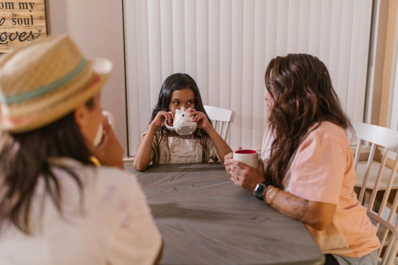 A warm family moment with three people enjoying drinks at the kitchen table.
