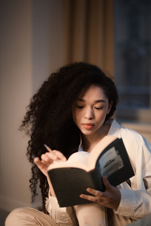 Free Young woman with curly hair reading a book indoors, captured in a calm and relaxing setting. Stock Photo