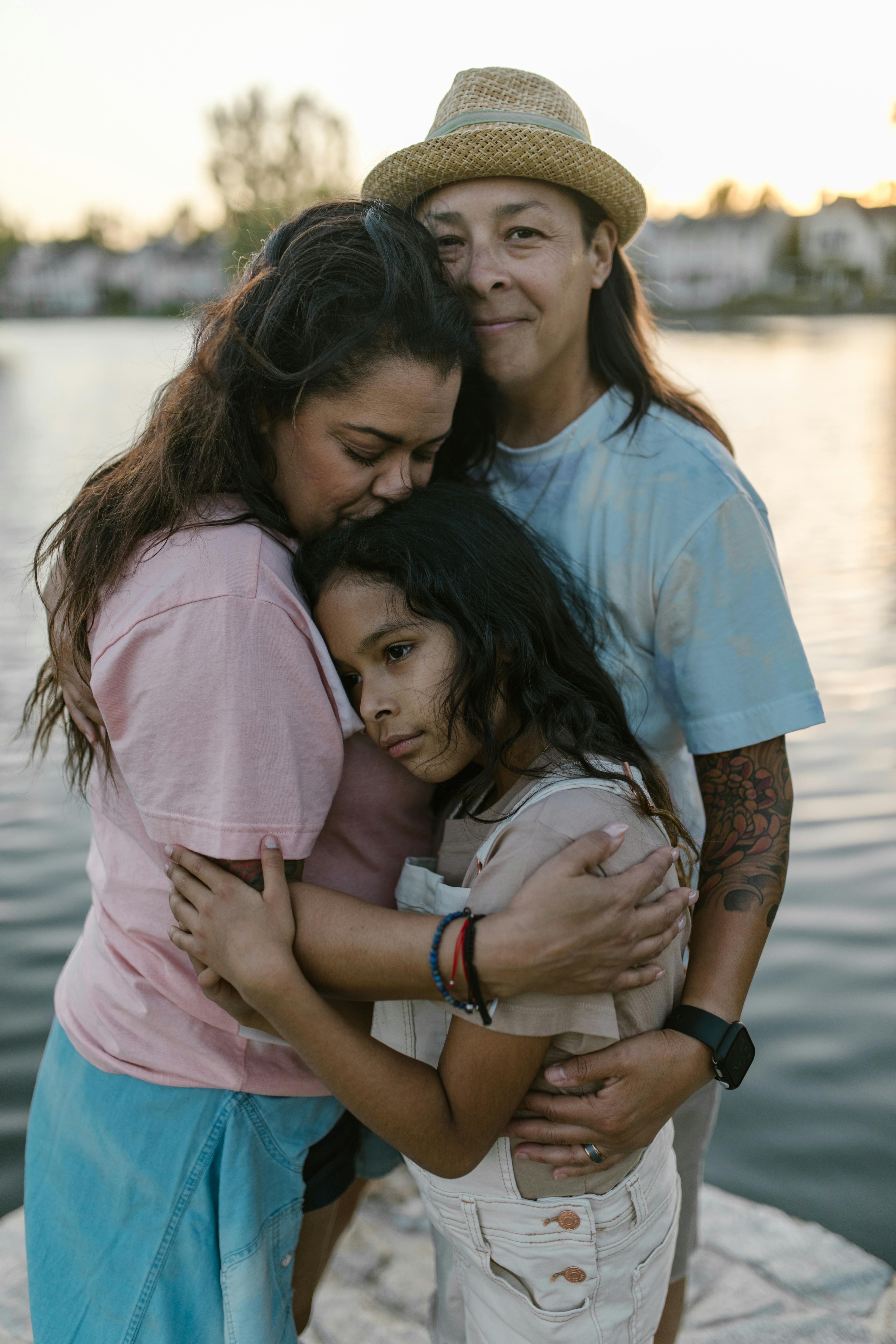 two women hugging a girl near a body of water