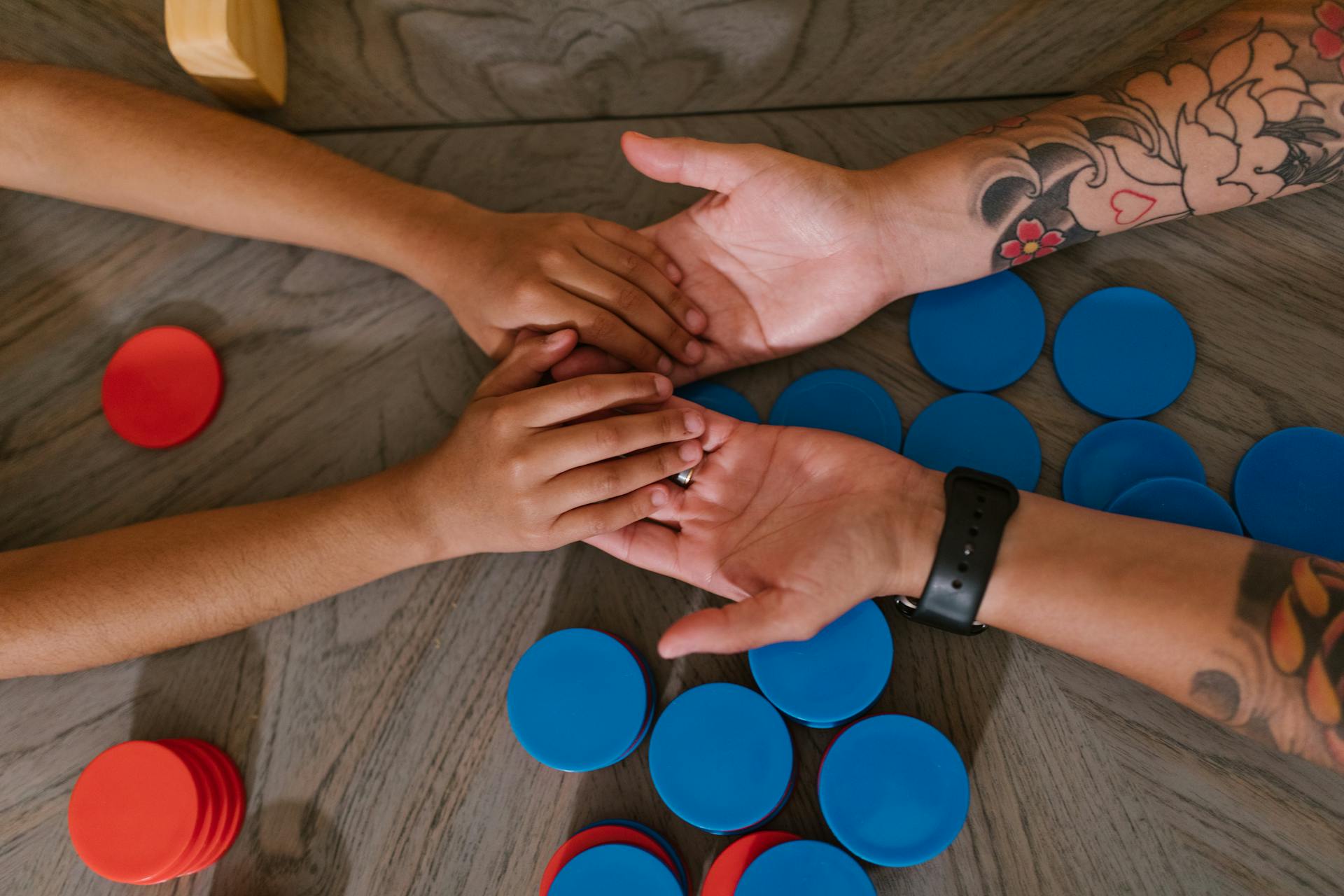 Top View of a Child and Person with Tattoos Holding Hands on the Table with Blue and Red Chips Lying Underneath